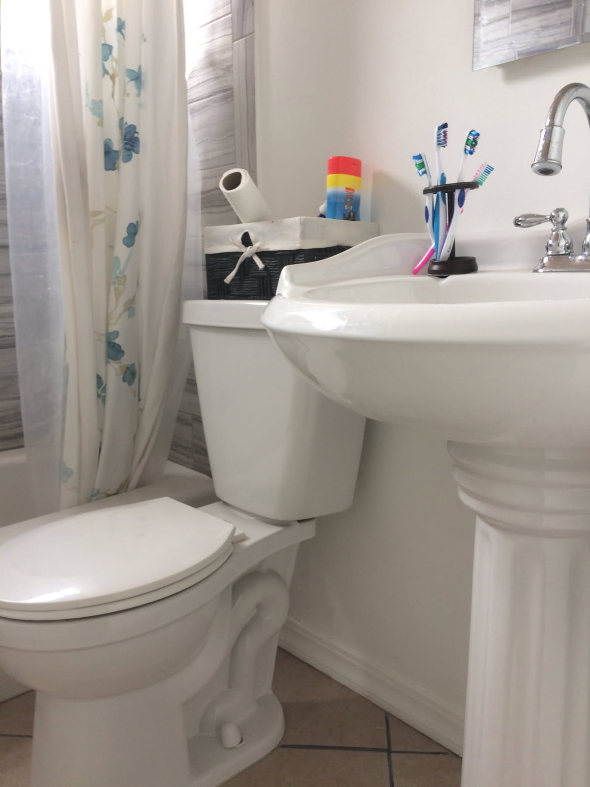 Clean bathroom with white pedestal sink, toilet, and shower curtain with blue leaf pattern