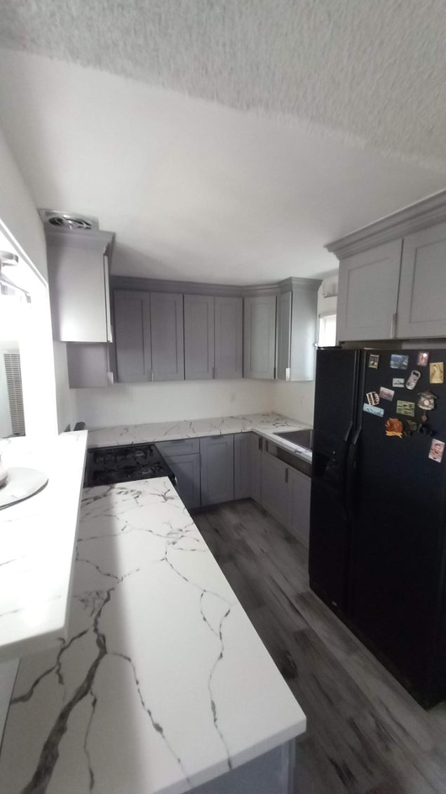 Modern kitchen with gray cabinetry, marble countertops, black appliances, and hardwood flooring