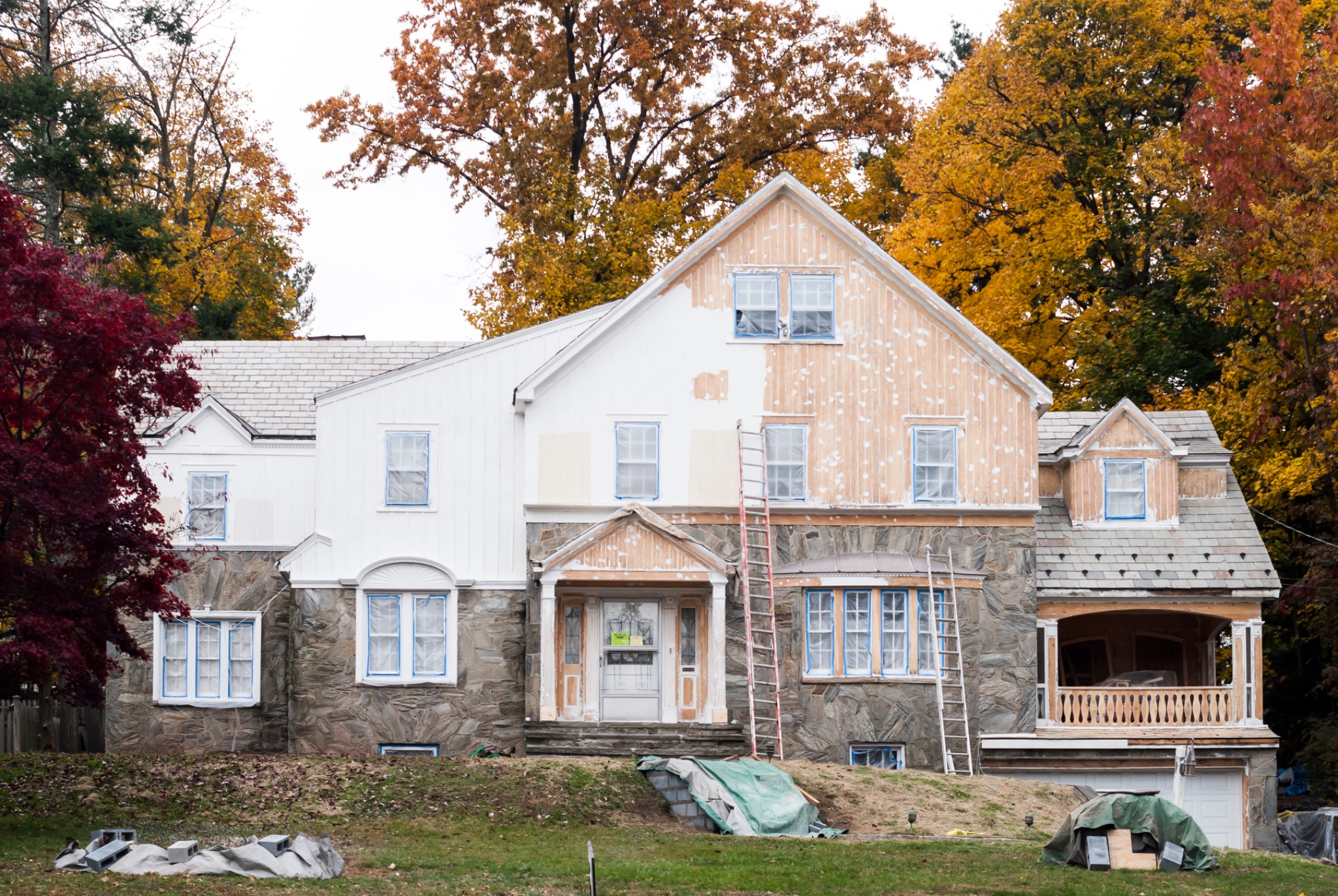 House undergoing exterior renovation with exposed wood siding and stone foundation in autumn